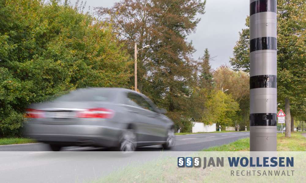 Stationäre Blitzeranlage PoliScan Speed an einer Straße in Flensburg, davor ein fahrendes Auto.